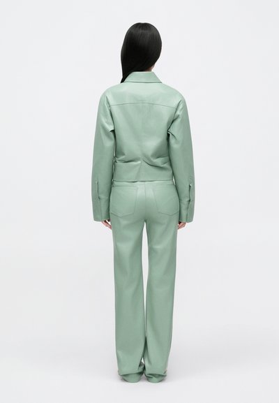 Conjunto de jaqueta e calças de couro verde menta, jaqueta curta com mangas longas e calças largas, apresentando bolsos traseiros e textura suave.