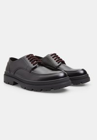 Scarpe in pelle nere con lacci rossi, punta rotonda e suola in gomma spessa con un motivo di battistrada testurizzato.