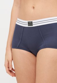 Tamnoplave bokserice od mekanog materijala, s bijelom elastičnom trakom u struku s crnim prugama i oznakom "B.T.B. UNDER WEAR."