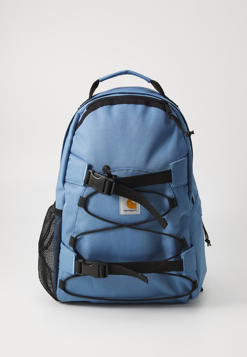 Blauer Stoffrucksack mit schwarzen Trägern, einer vorderen Netztasche und einem Logoschild. Verfügt über Schließschnallen und mehrere Verstellpunkte.