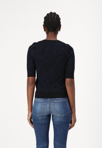 Marinblått strukturerat tröja med korta ärmar, blommönster och ribbad nederkant. Kombinerad med åtsittande jeans i denim, vilket visar en avslappnad outfit.