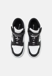 Svarte og hvite høy-top sneakers med lærøvre, polstret krage, perforert tå og svarte snørebånd; har et Champion-logo på tungen.