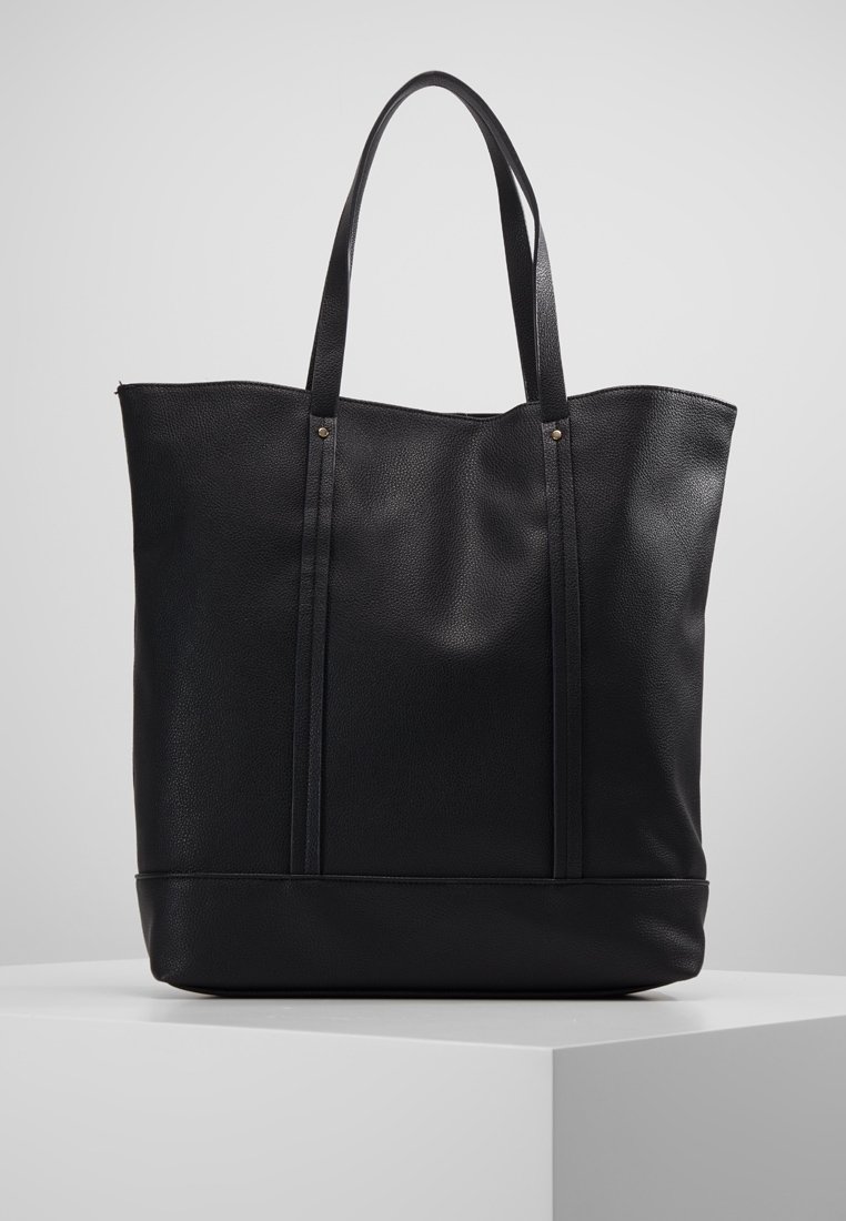 Sac fourre-tout en cuir noir à finition texturée, doté de deux longues poignées, d'une forme structurée et d'éléments de design minimalistes.