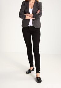 Grijze blazer, witte top, zwarte skinny jeans en zwarte instappers. Kenmerken zijn een getailleerde pasvorm en een soepele textuur. Eenvoudige ontwerpelementen aanwezig.