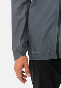 Giacca grigia scura con superficie strutturata. Presenta polsini elastici, chiusura con zip e loghi stampati, incluso "CEPLEX ADVANCED."