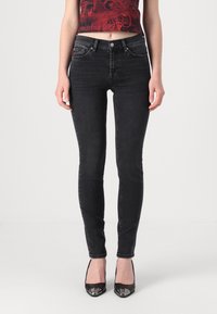 Jeans ajustados negros hechos de denim, con una textura suave y un diseño clásico de cinco bolsillos. Combinados con tacones negros de punta afilada.