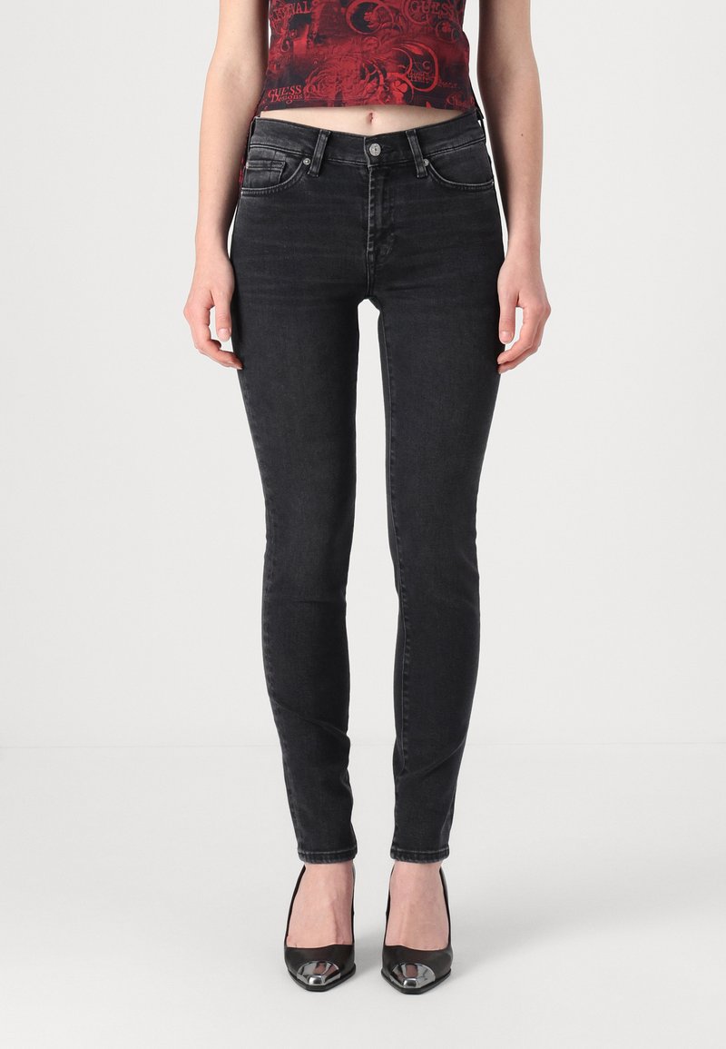 Jeans ajustados negros hechos de denim, con una textura suave y un diseño clásico de cinco bolsillos. Combinados con tacones negros de punta afilada.