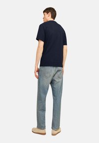 Navy blue cotton t-shirt with a relaxed fit, paired with light wash straight-leg denim jeans and beige slip-on shoes.