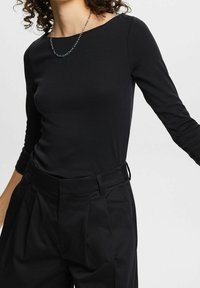 Czarna bluzka z długim rękawem wykonana z miękkiego materiału z okrągłym dekoltem. W zestawie z czarnymi spodniami o wysokim stanie z zakładkami.