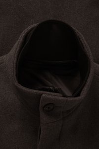 Bruine wollen jas met een hoge kraag, knoopsluiting en een binnenzak met rits. De binnenkant heeft een gladde zwarte voering.