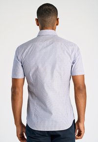 Camicia azzurra a maniche corte con righe verticali e motivi a pois rossi. Presenta un colletto classico e un orlo curvo per una vestibilità sartoriale.