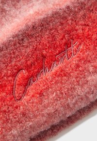 Gorro de punto con degradado en rojo, hecho de un material esponjoso y texturizado. Presenta un logotipo de la marca bordado en un tono contrastante.