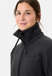 Zwarte fleece jack met een hoge kraag, een ritssluiting aan de voorkant en trekkoordaccenten. Beschikt over een subtiele logo op de borst en een zachte textuur.