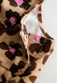 Samtstoff mit braunem und pinkfarbigem Blumenmuster, der einen Druckknopfverschluss und einen gefalteten Saum eines Kleidungsstücks zeigt.