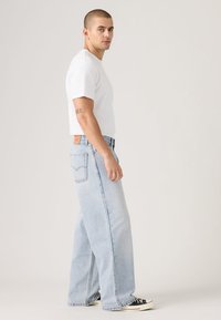 Light blue denim jeans with a loose fit, featuring front and back pockets, contrasted stitching, and a brown leather tag at the waistband.