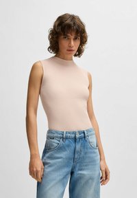 Ribbed, sleeveless top in light pink, featuring a high neck. Paired with light blue denim jeans with a faded finish and five-pocket design.