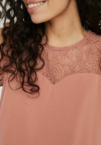 Pink dress featuring a lace yoke with a scalloped edge, short sleeves, and a soft, flowing fabric texture. Curly hair is visible.