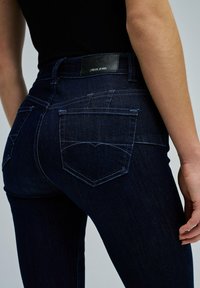 Jeans de mezclilla de un índigo oscuro con un diseño ajustado y costuras en contraste. Cuenta con dos bolsillos traseros, una etiqueta de cuero con la marca y piernas ajustadas.