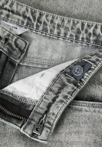 Jean en denim gris avec une taille repliée à imprimé animal subtil, fermeture à boutons et doublure beige visible à l'ouverture.