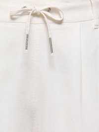 Gros plan de la ceinture d'un pantalon blanc avec un cordon en tissu noué présentant des embouts métalliques et des détails cousus.