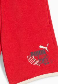 Rode stof met het Puma-logo, gestileerde hardloopschoen grafiek en witte gebogen lijnen nabij de onderrand.