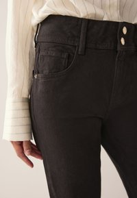 Čierne džínsy s vysokým pásom a hladkou textúrou. Majú dve zlaté gombíky a bočné vrecká. Nosené s ľahkým pruhovaným dlhým rukávom.