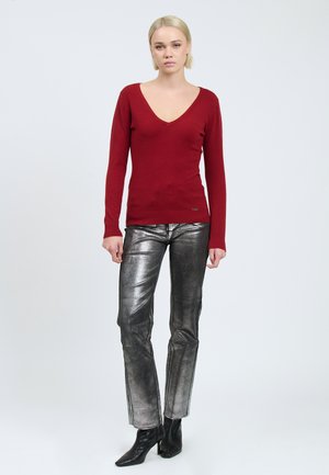 Rode v-hals trui met lange mouwen, gecombineerd met metallic zilveren rechte broek en zwarte enkellaarzen. Gladde textuur en getailleerd ontwerp.