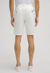 White cotton shorts with a smooth texture, featuring a classic cut, side pockets, and buttoned back pockets. Rolled hem with subtle stitching.