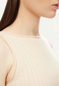 Hudfärgad ribbad linne med rund halsringning. Tyget har en mjuk textur och en subtil lyster, utformat för en figurnära silhuett.
