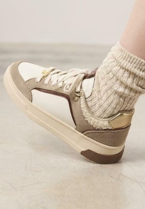 Baskets beiges et blanches avec fermeture à lacets, en cuir suédé et cuir, accents texturés, et détail de talon doré.