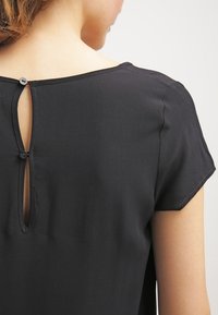 Czarny top z krótkim rękawem o okrągłym dekolcie, z tyłu z otworem w kształcie klucza i zapięciem na guzik. Gładki materiał z delikatnym połyskiem.
