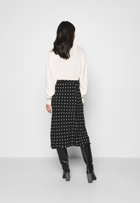 Jupe midi noire à pois, au design fluide, associée à un pull en tricot crème avec des détails texturés et des manches ballon. Bottes à talons noires.