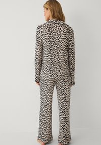 Klæd dig i leopardmønstret pyjamas-sæt i sort og beige farveskema, der omfatter en skjorte med knapper og flared bukser i blødt, tekstureret stof.