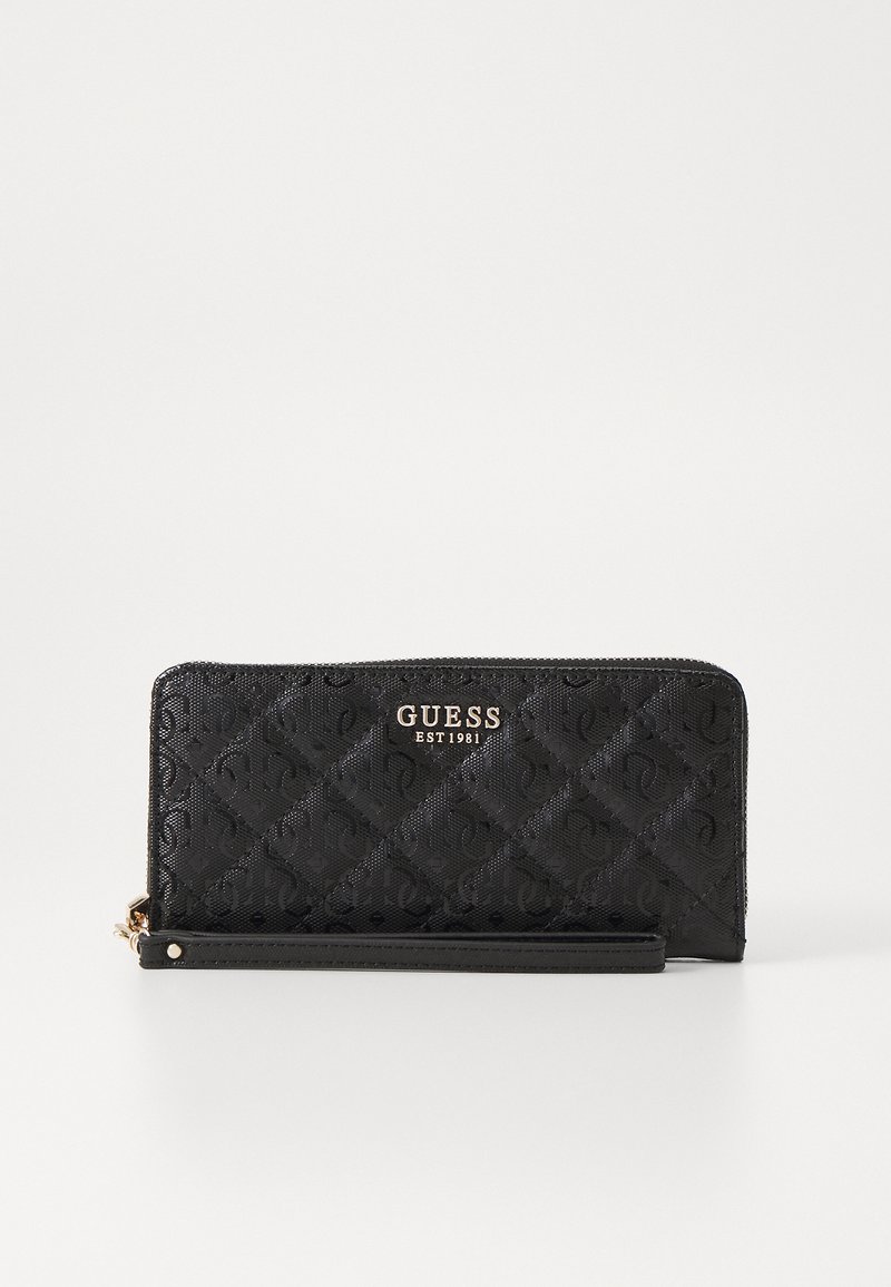 Cartera sintética negra acolchada que presenta un logo dorado "GUESS EST 1981". Diseño slim con cierre de cremallera y correa para la muñeca desmontable.