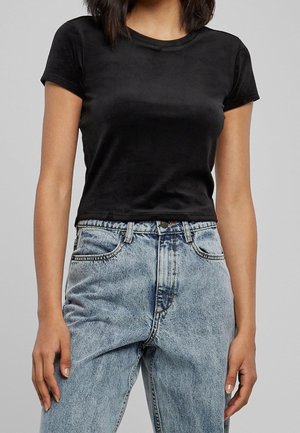Vrouw draagt een aansluitend zwart T-shirt met korte mouwen, ingestopt in een hooggetailleerde lichtblauwe spijkerbroek met knoop- en ritssluiting.