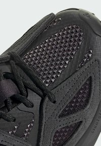 Čierna športová obuv s textúrovaným zvrškom a sieťovanými panelmi, kombináciou hladkých a semišových materiálov. Výrazný geometrický dizajn.