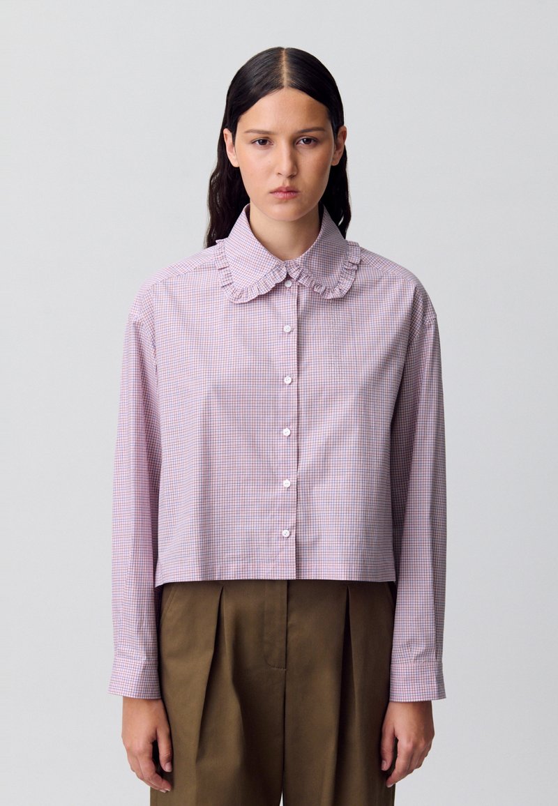 Camisa recortada de botones en cuadros rosa y blanco. Presenta un cuello con volantes y mangas largas. Tela de algodón texturizado.