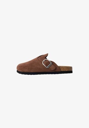 Brown suede clogs with a silver buckle, open back, cork sole, and textured finish. Features a rounded toe and flat, non-slip base.