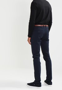 Mörkblå chinos med smal passform, tillverkade av bomull, med ett bälte med en brun läderdetalj. Strukturerad midjeband och bakfickor.