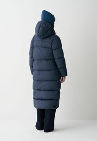 Marinblå puffjacka med horisontellt quiltade segment, huva och långa ärmar, tillsammans med en ribbad blå mössa. Avslappnad, ledig passform.