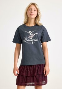 Sort t-shirt med en ballerina grafik i pink og hvid, parret med en lagdelt burgunder blonde nederdel, der fremviser ruffles og delikat tekstur.