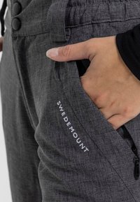 Grå tygbyxor med elastisk midja, dragkedjefickor och broderad "SWEDMOUNT"-logga på sidan. Texturerad yta synlig.