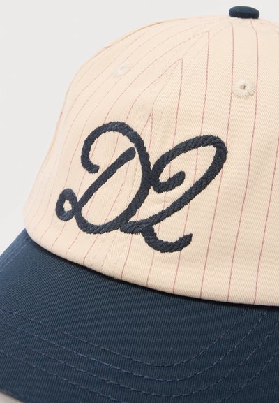 Μπεζ και μπλε καπέλο бейзμπολ με λεπτές κόκκινες ρίγες και ένα μεγάλο κεντημένο στυλιζαρισμένο "DL" σε σκούρο μπλε χρώμα στην μπροστινή επιφάνεια.