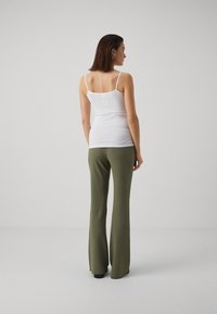 Débardeur blanc ajusté avec des fines bretelles associé à un pantalon large texturé vert olive. La vue de dos met en avant le design simple de la tenue.