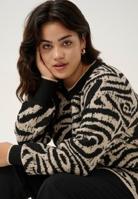 Pulover tricotat cu un model abstract în nuanțe de negru și bej, având guler rotund și manșete côté. Textură moale și croială lejeră.