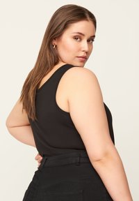 Top negro sin mangas con escote redondo, tejido texturizado, diseño ajustado y acabado suave, combinado con pantalones negros de cintura alta.
