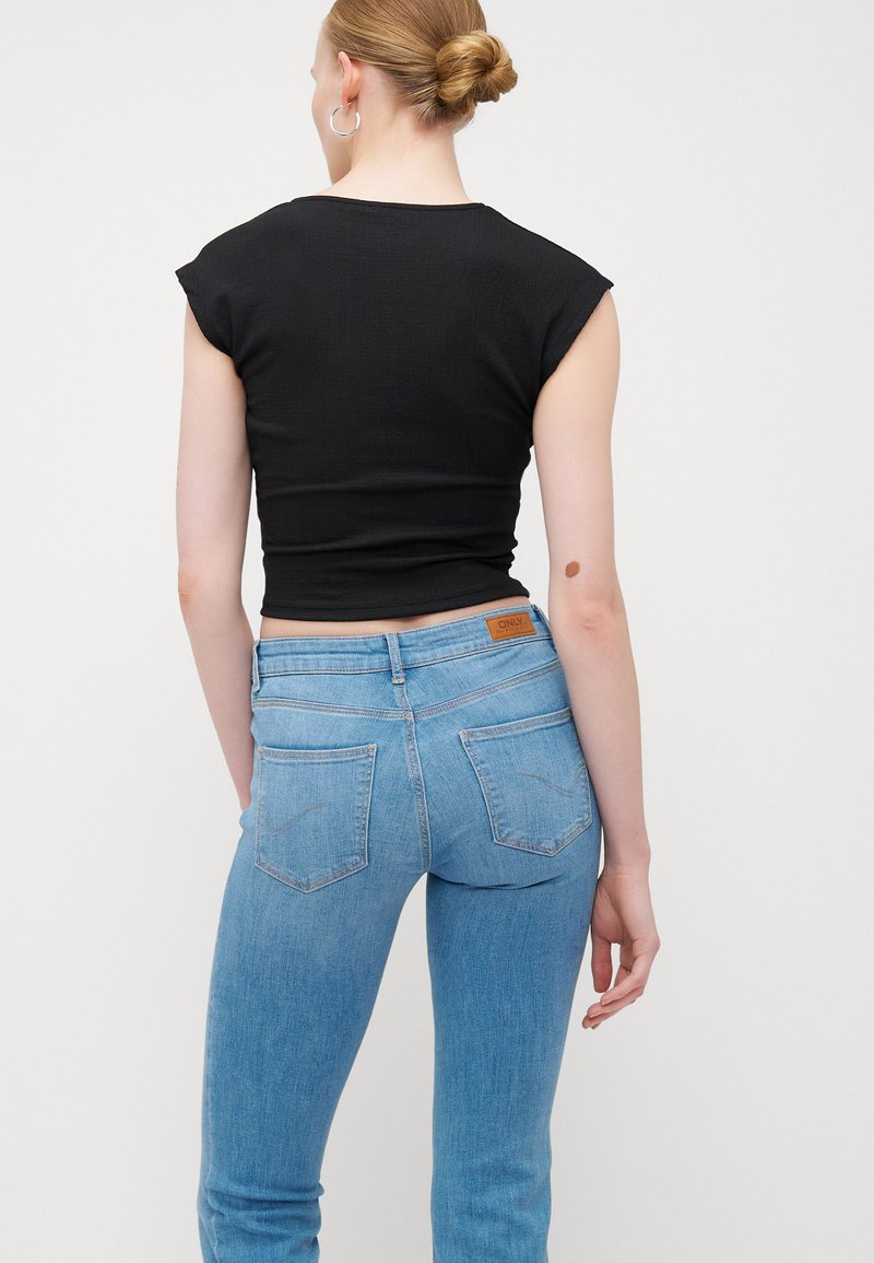 Schwarzes figurbetontes Oberteil mit kurzen Ärmeln und hoher Taille, kombiniert mit hellblauen Jeans aus Denim, die über Gesäßtaschen und ein braunes Lederetikett verfügen.