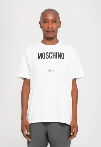 Fehér póló, amelynek elején fekete, vastag betűkkel szerepel a "MOSCHINO" felirat, alatta pedig a "Milano" felirat található, rövid ujjakkal és laza szabással.