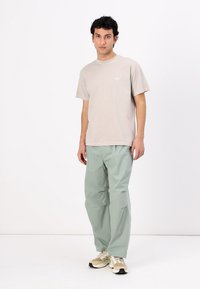 Světle béžové tričko s malým logem, spárováno s volnými světle mátovými kalhotami. Model má na sobě béžové tenisky. Jednoduchý, neformální outfit.