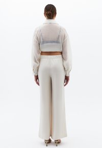 Kort, genomskinlig vit blus med långa ärmar och knapplösningar, i kombination med högmidjade, vida byxor i matchande nyans.